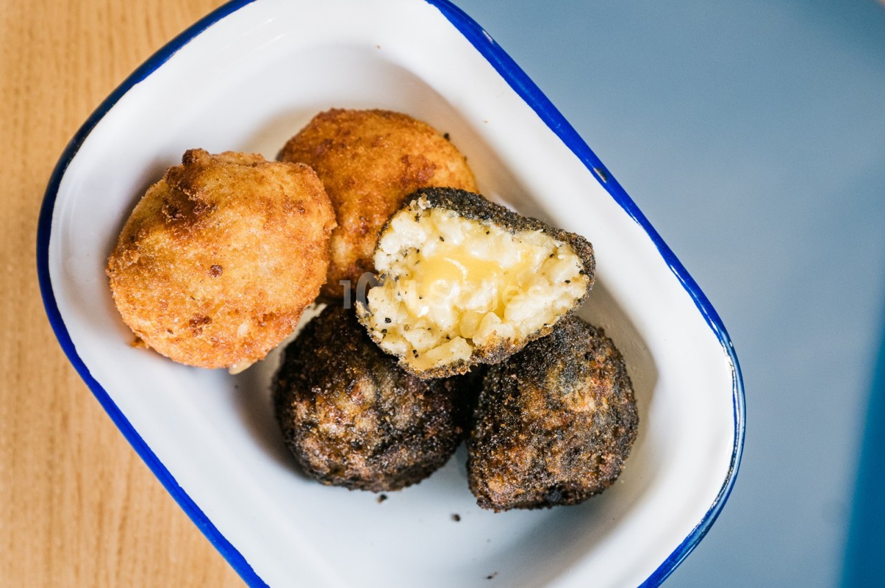 Boulettes panées dorées et noires, dont une ouverte révélant un cœur fondant au fromage, servies dans un plat émaillé.