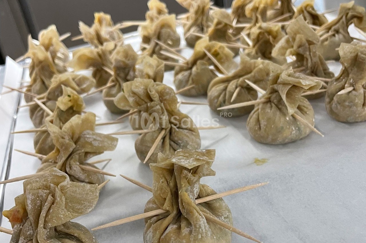Raviolis en forme de bourses fermées avec des cure-dents, disposés sur une surface blanche.