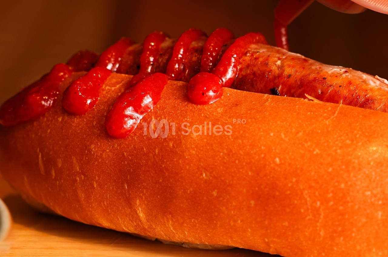 Saucisse grillée dans un pain allongé, garnie de ketchup en zigzag.