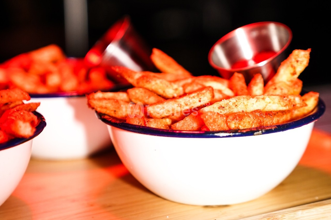 Bol de frites dorées assaisonnées, servi avec une petite coupelle en métal sur une table en bois.