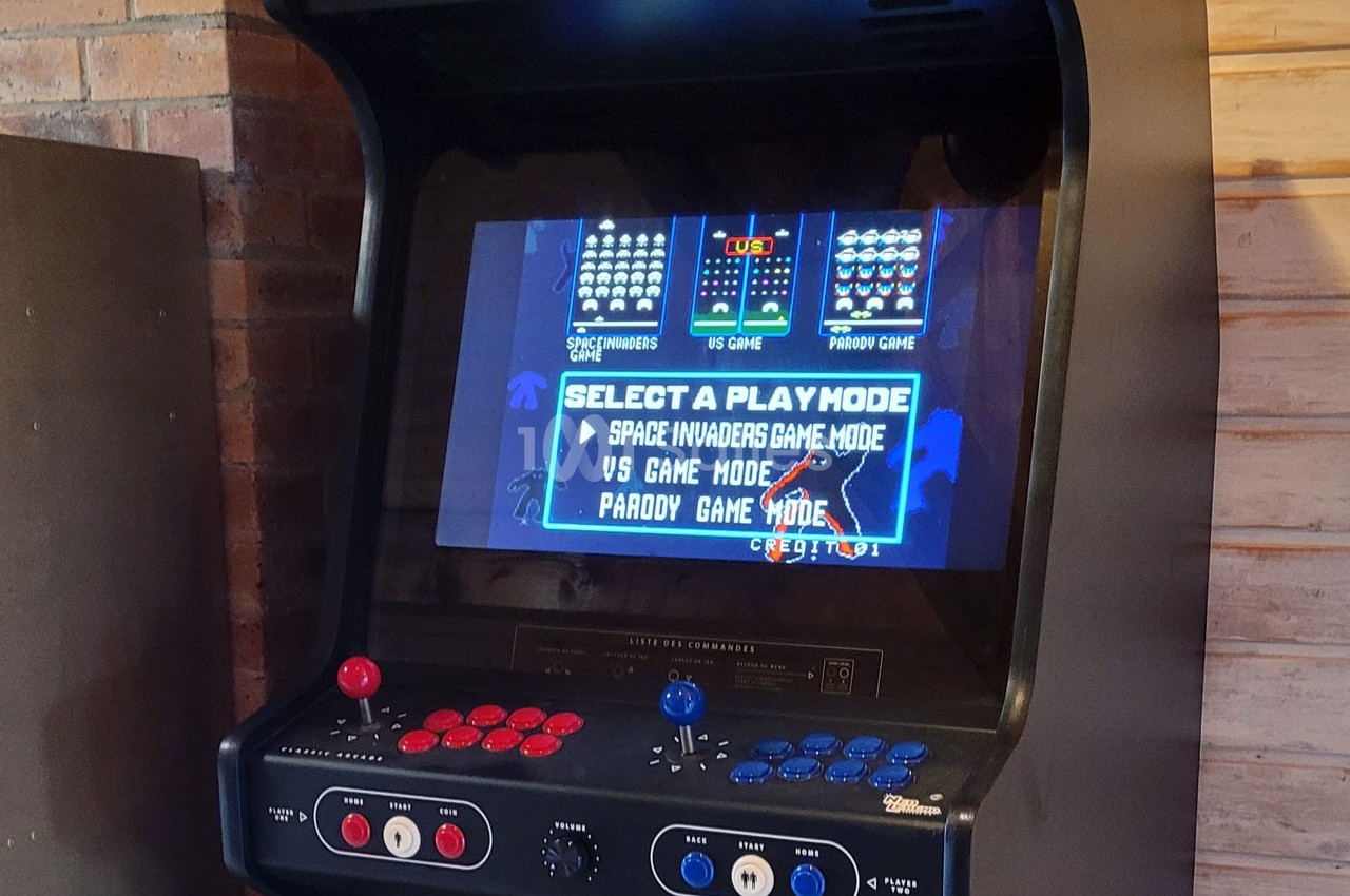 Borne d'arcade rétro affichant un écran de sélection de mode de jeu, avec boutons et manettes visibles.