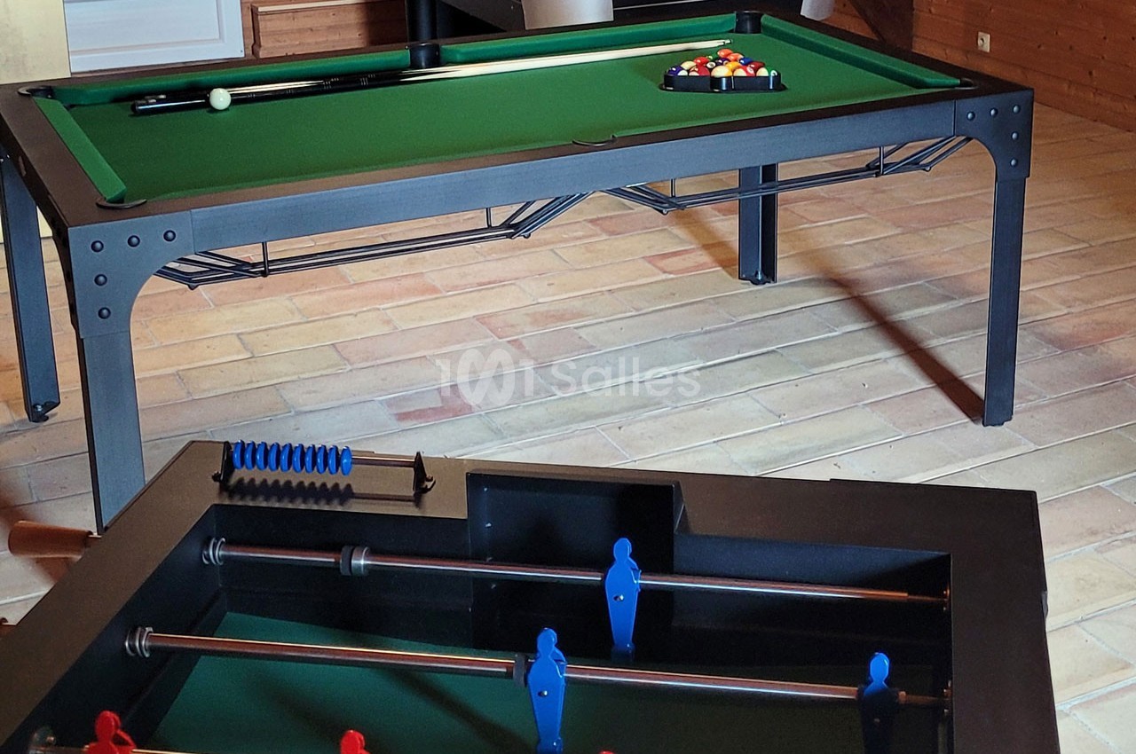 Table de billard avec triangle de billes colorées en arrière-plan et baby-foot en premier plan dans une pièce.