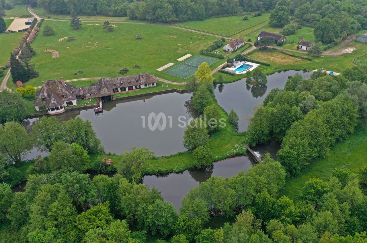 Vue aérienne d'un domaine avec étangs, bâtiments traditionnels, piscine et espaces verts entourés de forêt.