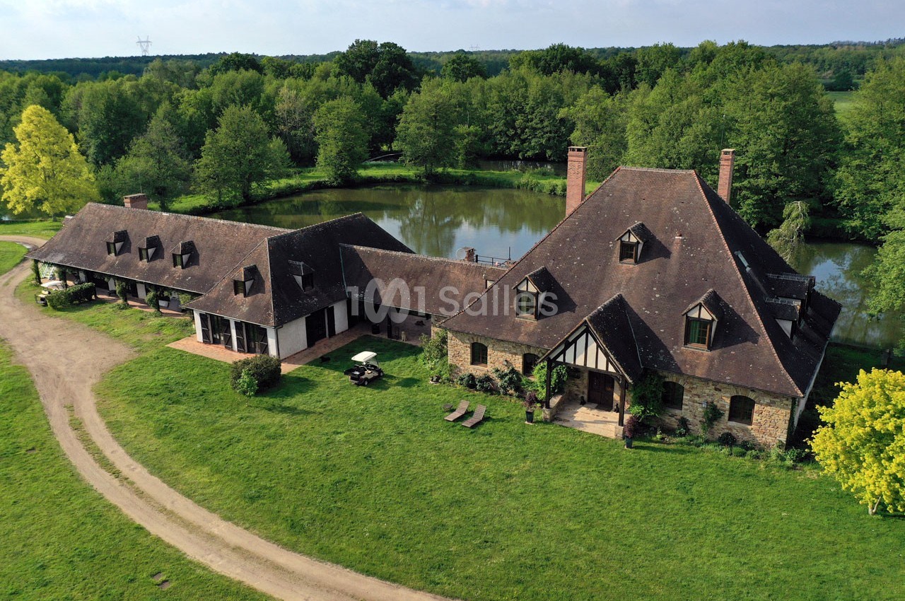 Vue aérienne d'une grande maison en pierre avec toit en ardoise, entourée de verdure et d'un étang.