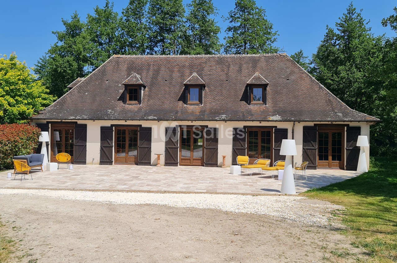 Maison traditionnelle avec toit en pente, terrasse aménagée de mobilier extérieur, entourée de verdure.
