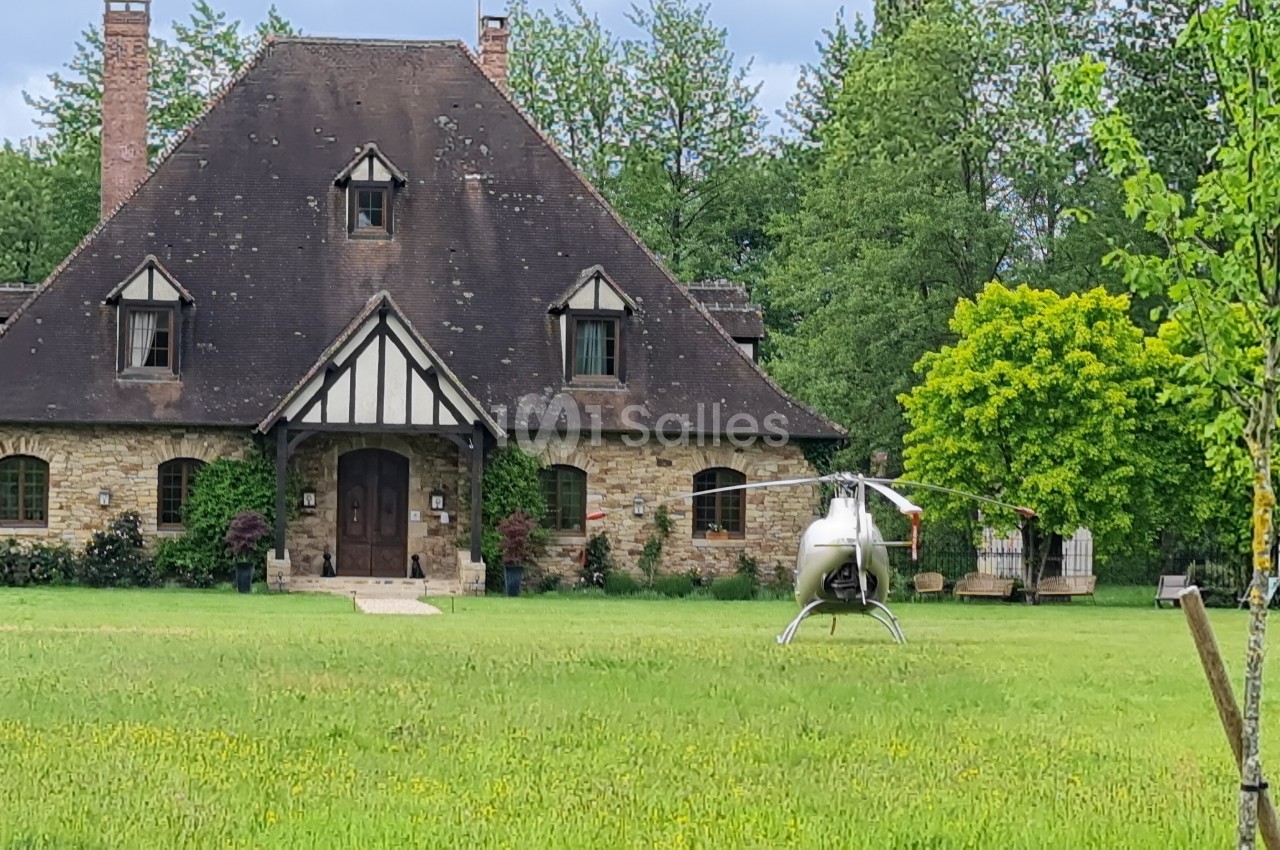 Hélicoptère posé sur une pelouse devant une grande maison en pierre entourée d'arbres.