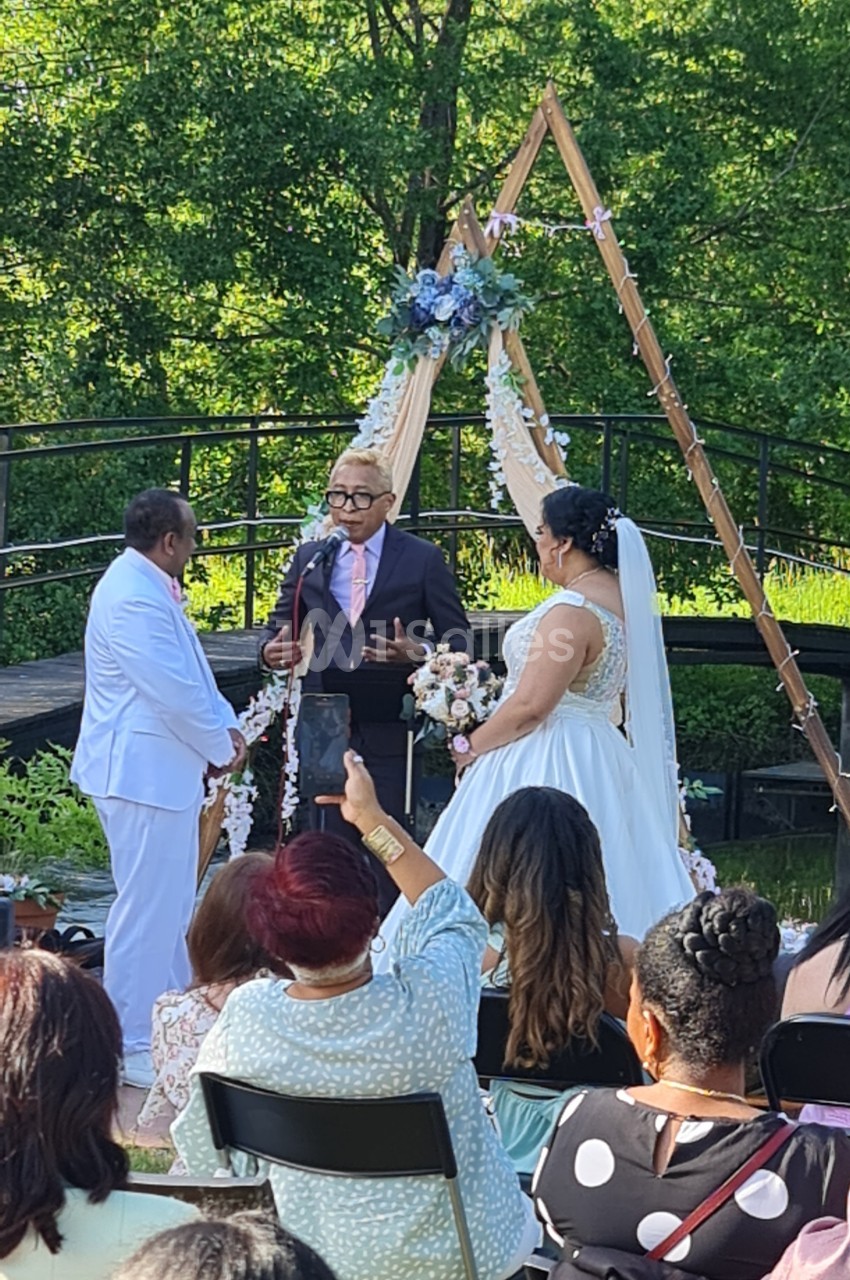 Un couple échange ses vœux devant un officiant lors d'une cérémonie de mariage en plein air.