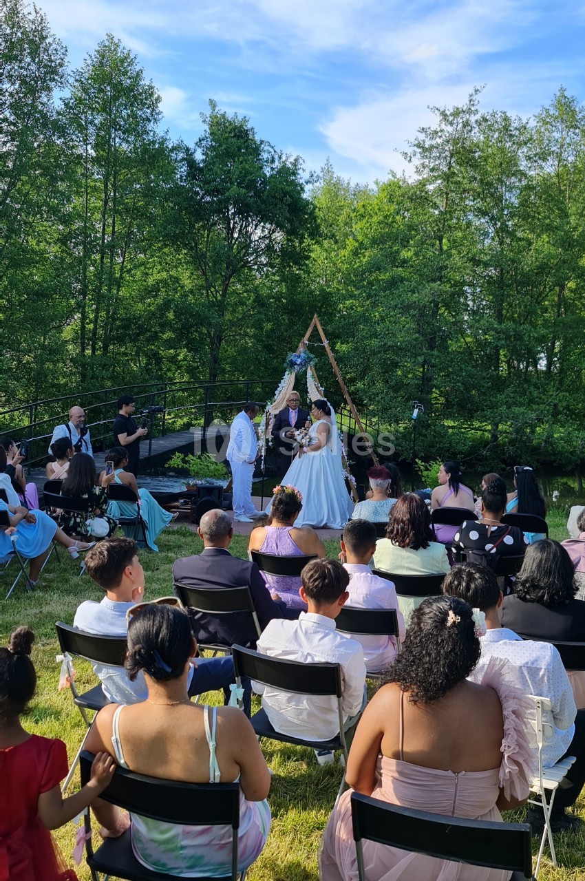 Cérémonie de mariage en plein air avec des invités assis, un couple échangeant ses vœux devant une arche décorée.