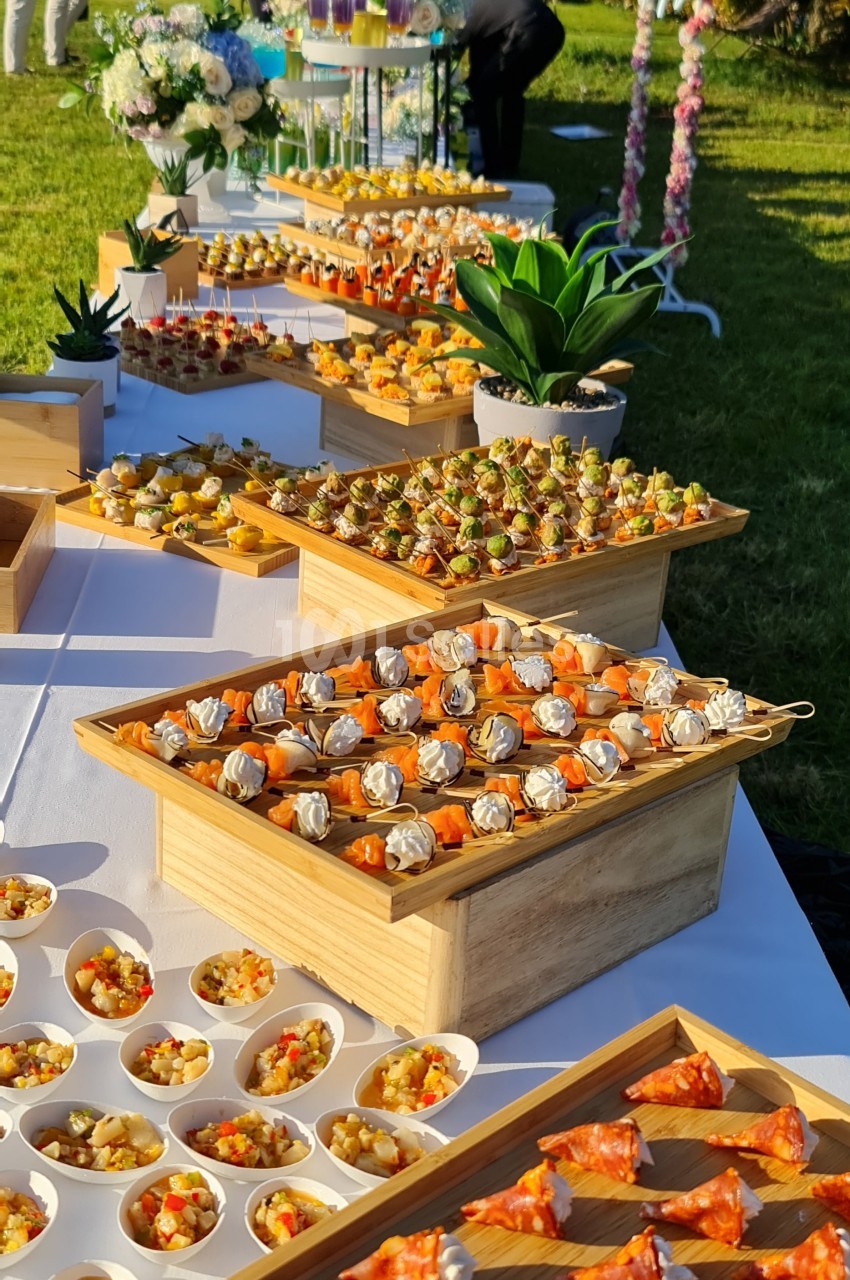 Buffet en plein air avec une variété de bouchées salées et sucrées présentées sur des plateaux en bois.