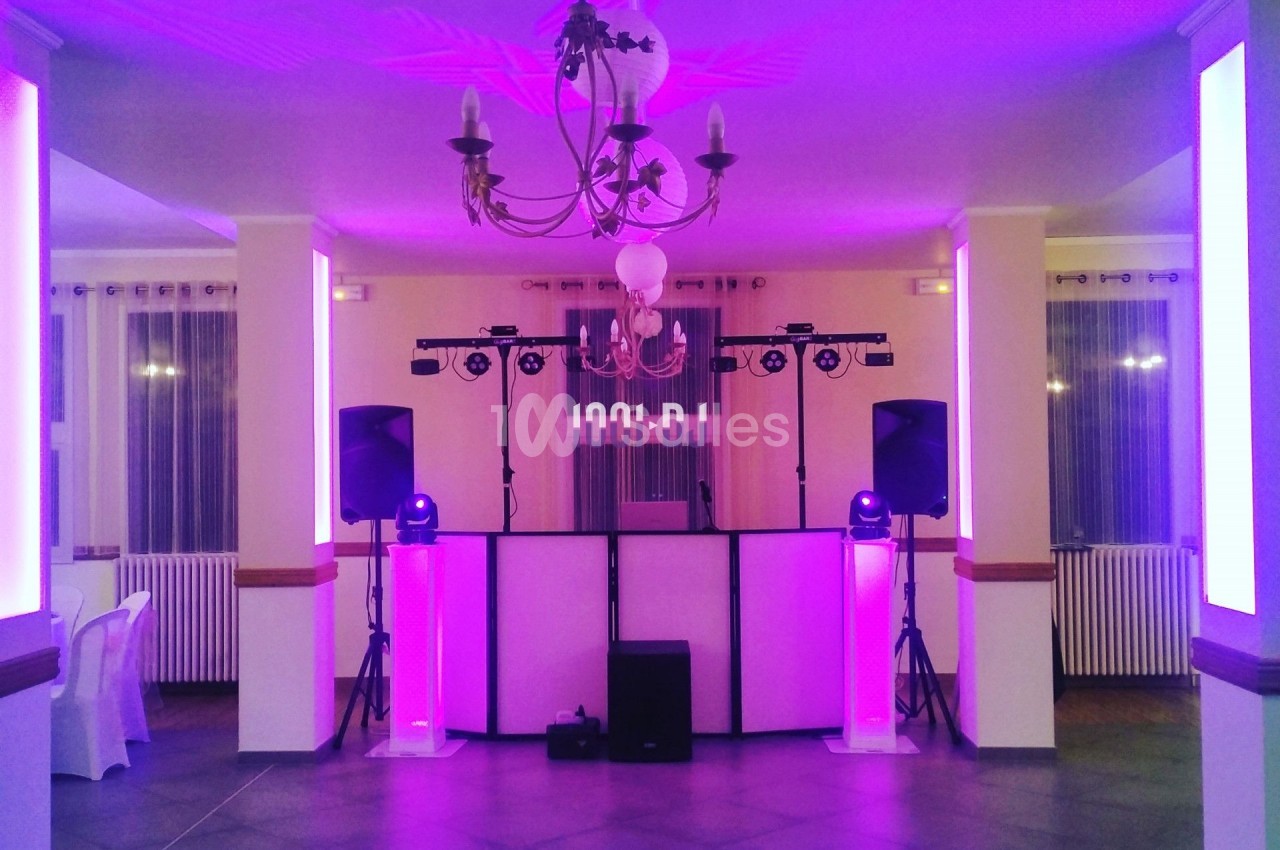 Salle de réception éclairée en rose avec une piste de danse, des enceintes et un équipement de DJ installé.