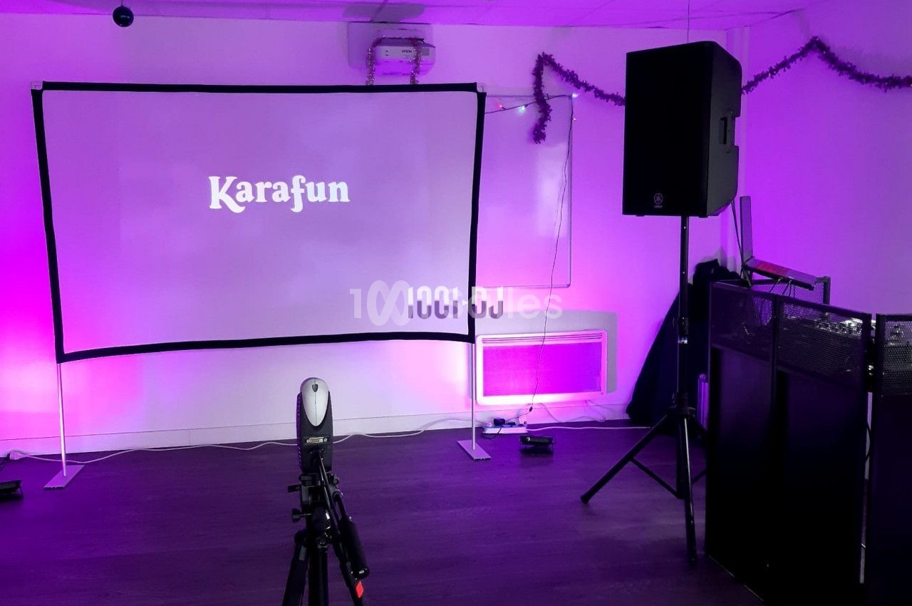 Écran de karaoké avec projecteur, haut-parleurs et décorations lumineuses dans une salle équipée.