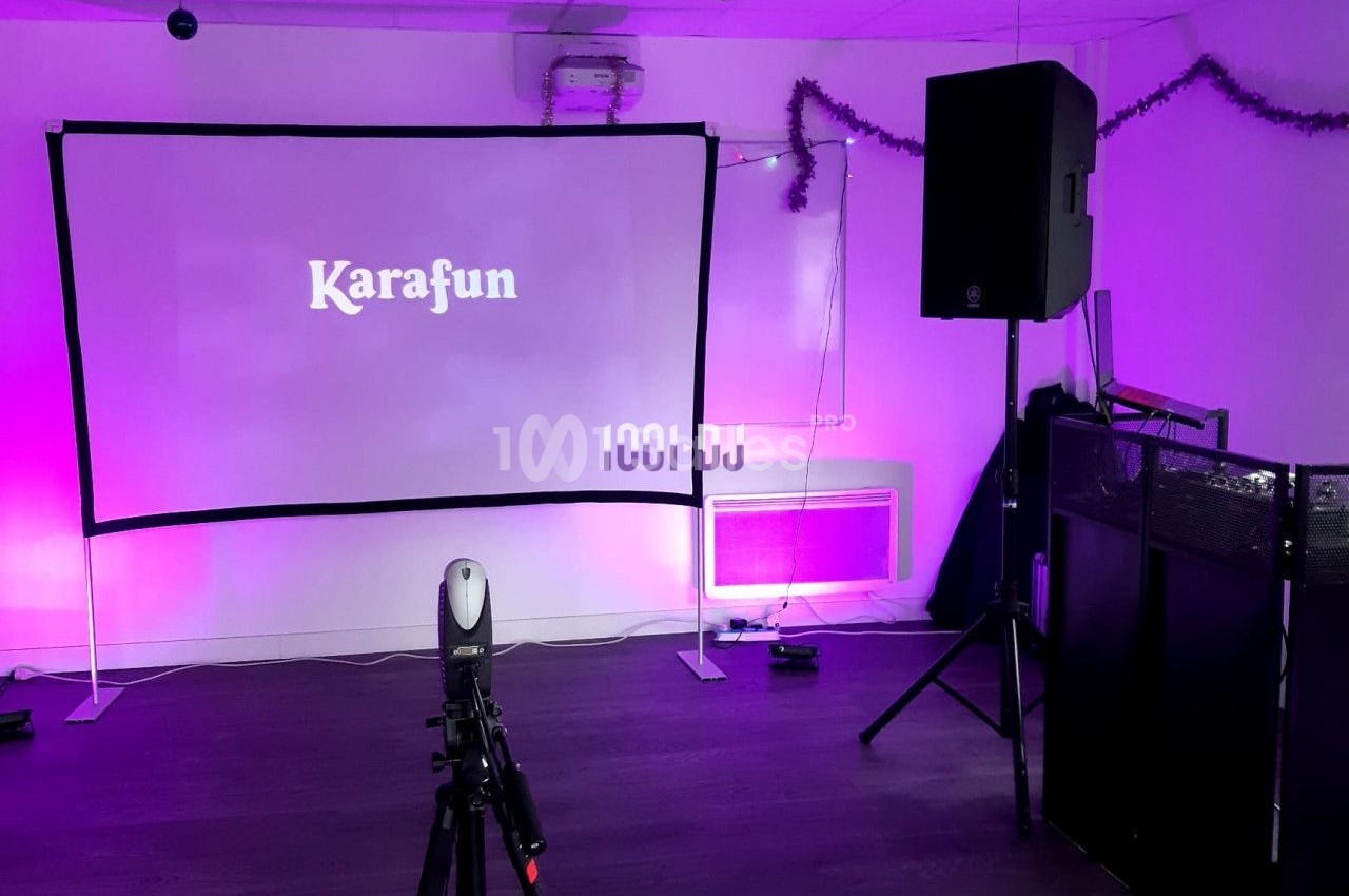Écran de karaoké avec projecteur, haut-parleurs et décorations lumineuses dans une salle équipée.