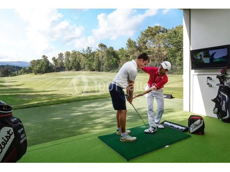 Un instructeur enseigne à un golfeur sur un tapis d'entraînement, avec un terrain de golf en arrière-plan.