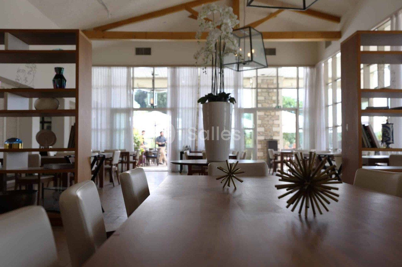 Salle de restaurant lumineuse avec grandes baies vitrées, tables en bois, chaises claires et décoration moderne.
