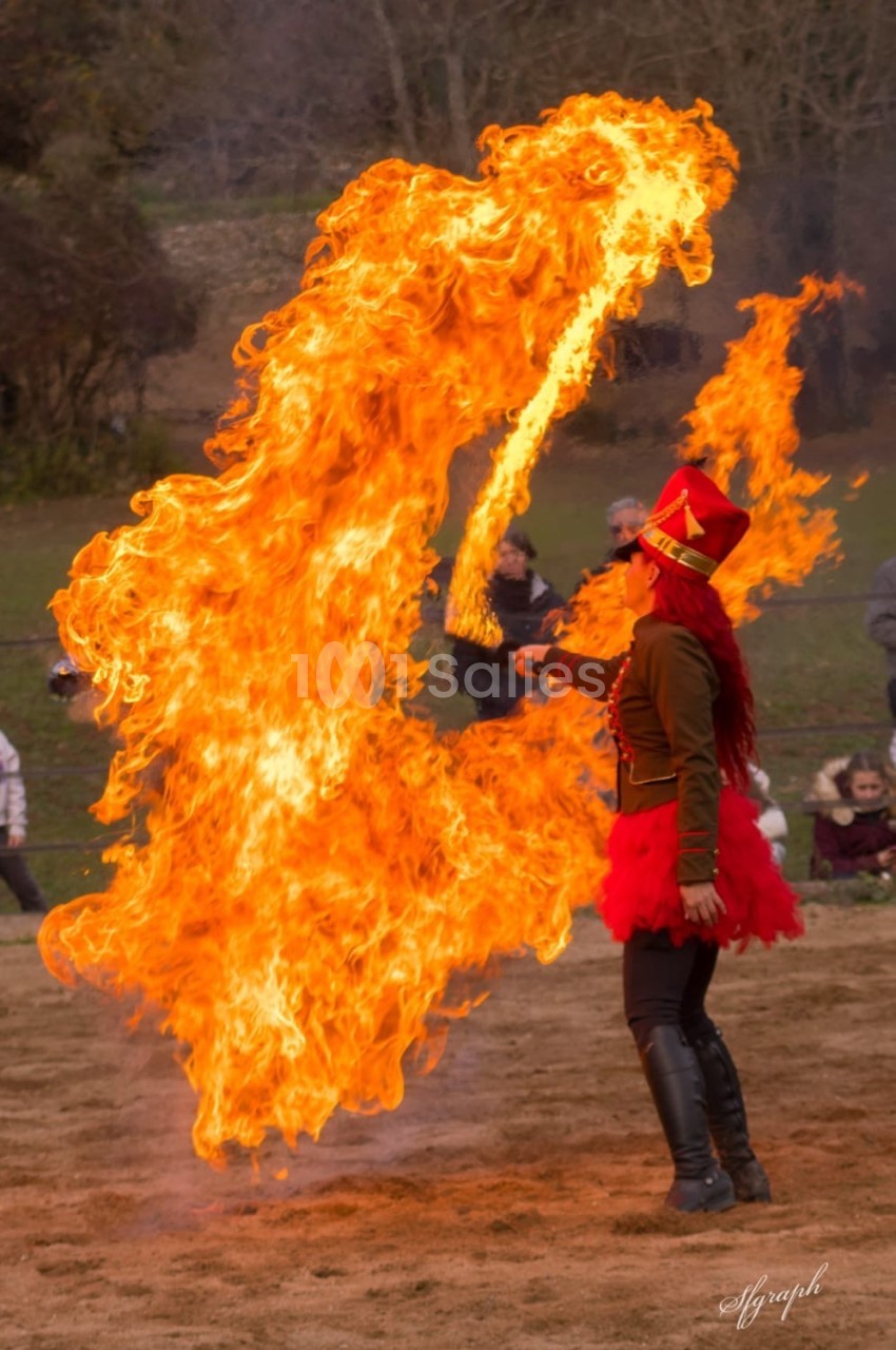 Une artiste en costume rouge manipule une grande flamme lors d'une performance en plein air.