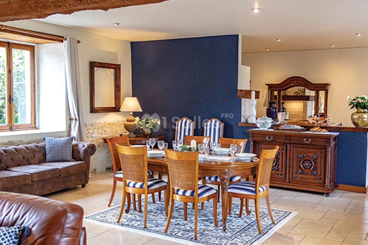 Salle à manger avec table en bois, chaises à rayures, buffet ancien, canapé et mur bleu dans un intérieur lumineux.