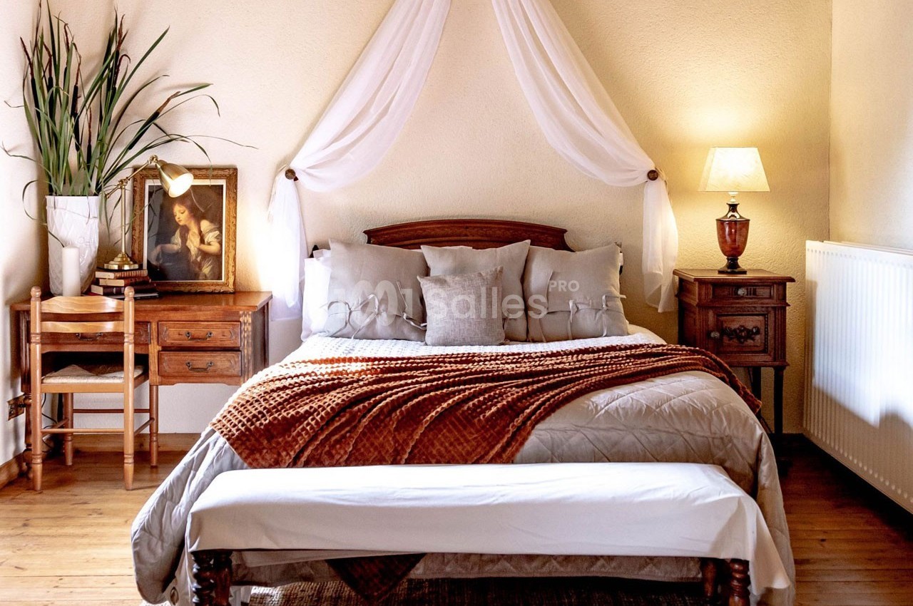 Chambre avec lit double, plaid orange, mobilier en bois, lampe allumée et décoration murale en tissu blanc.