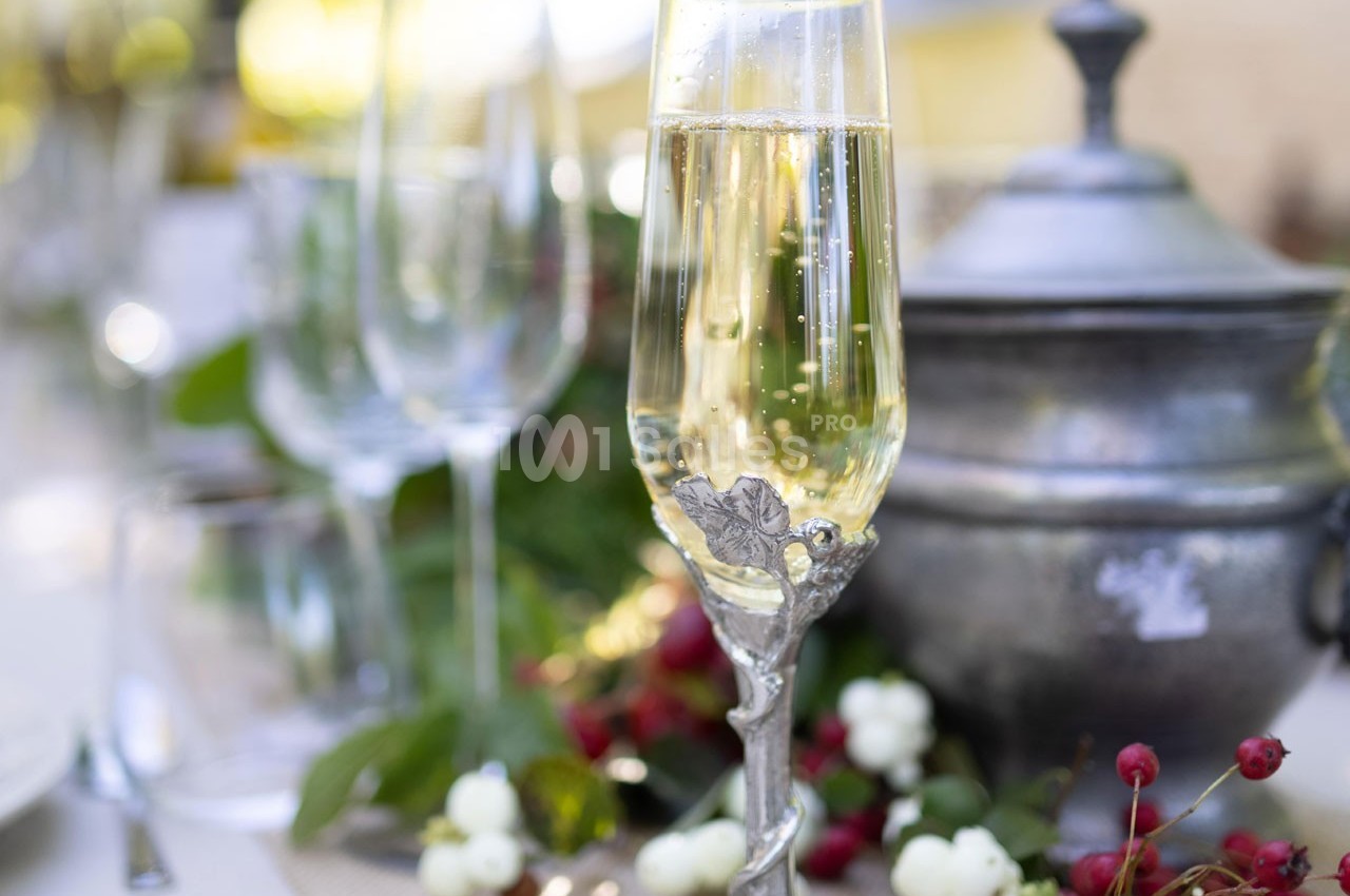 Verre de champagne décoré sur une table dressée avec des éléments naturels et une soupière en arrière-plan.