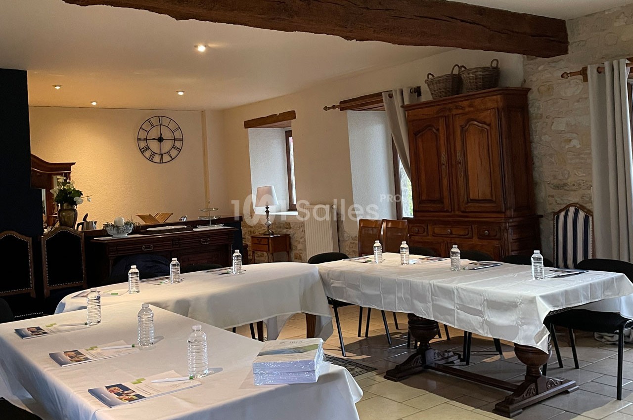 Salle de réunion lumineuse avec tables disposées en U, nappées de blanc, bouteilles d'eau et documents posés.