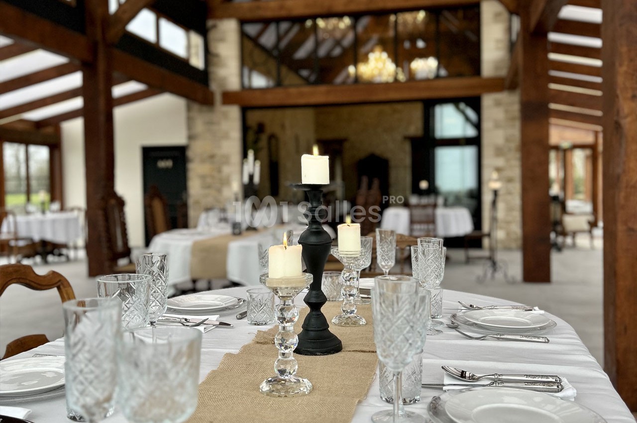 Table élégamment dressée avec chandeliers noirs, verres en cristal et nappes blanches dans une salle au style rustique.