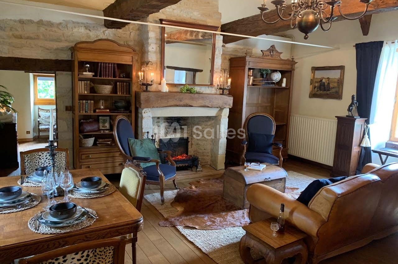 Salon rustique avec poutres apparentes, cheminée en pierre, mobilier en bois et fauteuils autour d'une table basse.