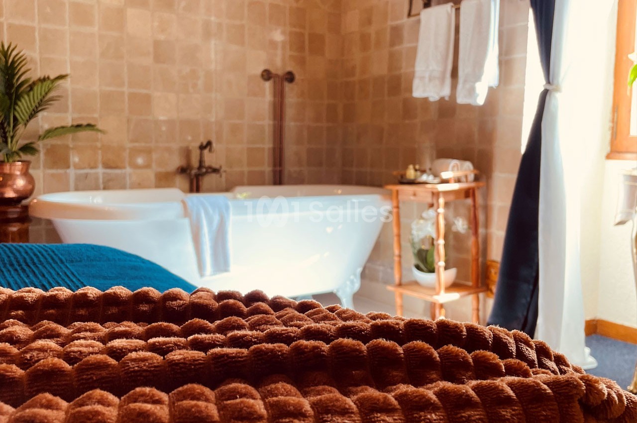 Salle de bain avec baignoire sur pieds, serviettes pliées au premier plan et lumière naturelle entrant par une fenêtre.