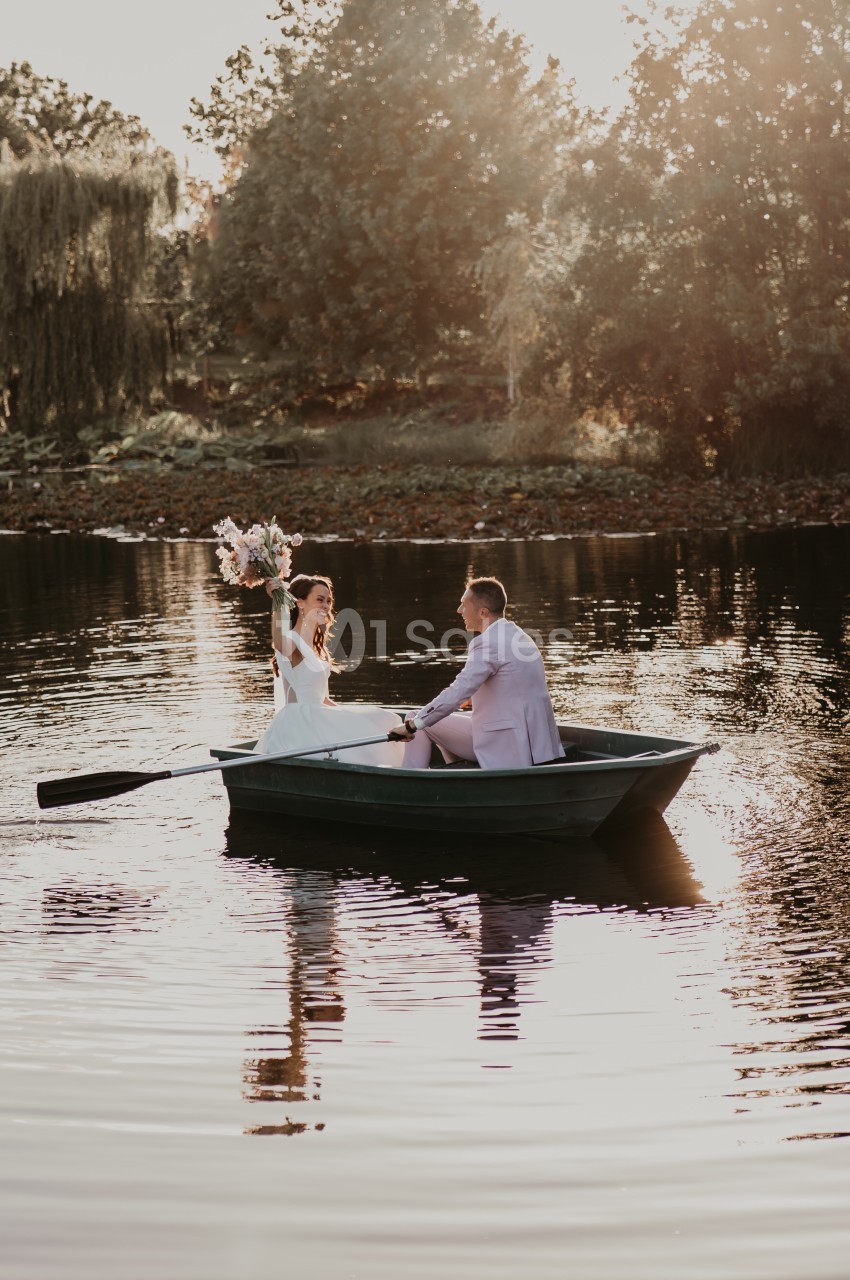 Un couple dans une barque sur un lac au coucher du soleil, la femme tenant un bouquet de fleurs.