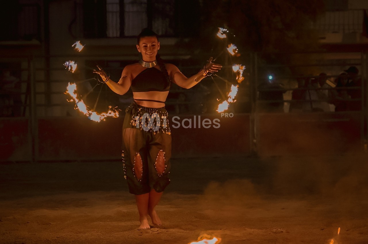 Une femme jongle avec des anneaux enflammés lors d'une performance nocturne en extérieur.