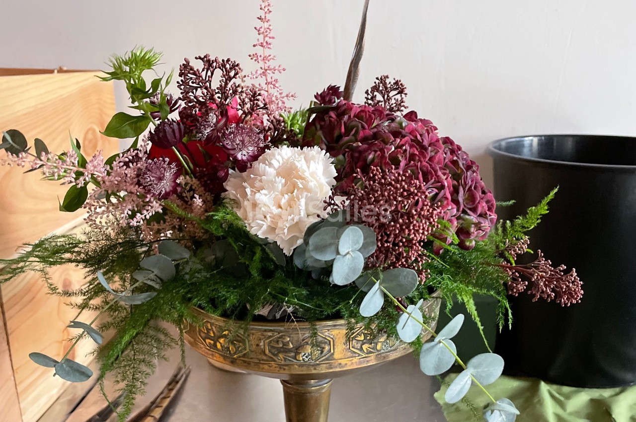Composition florale dans une coupe en métal doré, avec des fleurs rouges, blanches et feuillages verts.