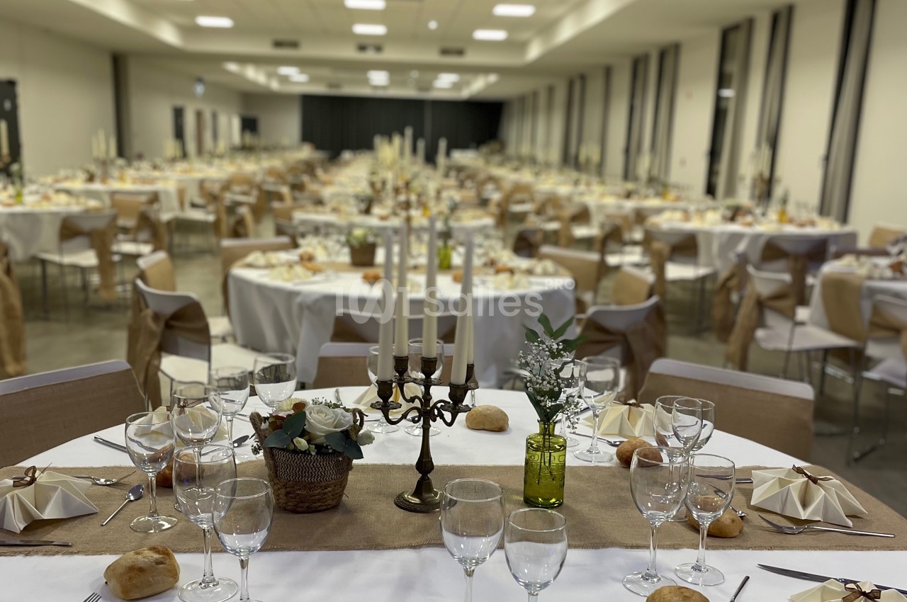 Salle de réception décorée avec des tables rondes dressées, nappes blanches et centres de table élégants.