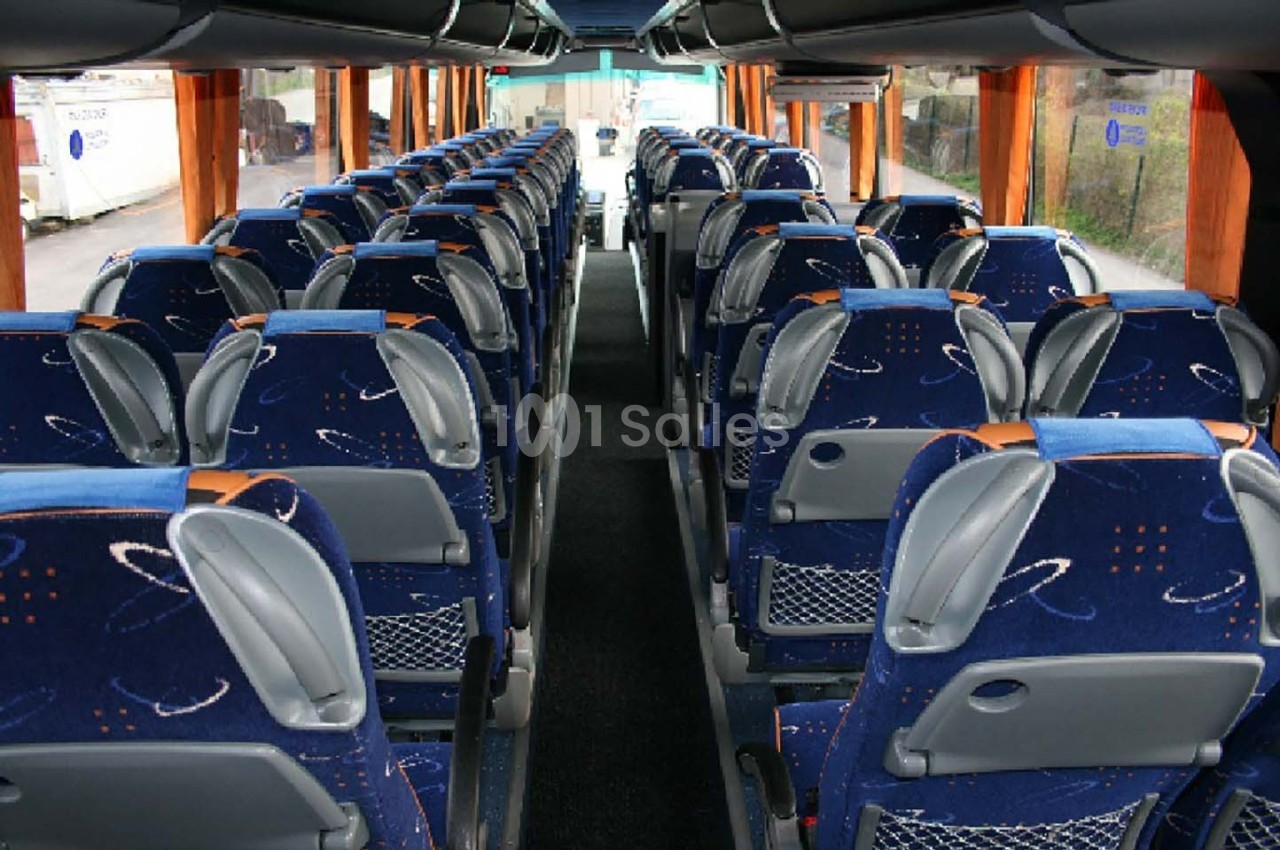 Intérieur d'un autocar avec des rangées de sièges bleus à motifs, couloir central et fenêtres latérales.