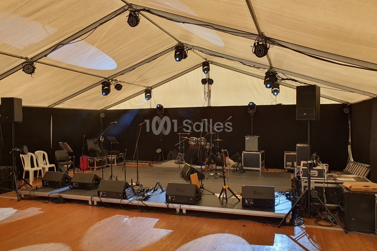 Scène vide sous un chapiteau, équipée de micros, enceintes, amplificateurs et batterie, prête pour un concert.
