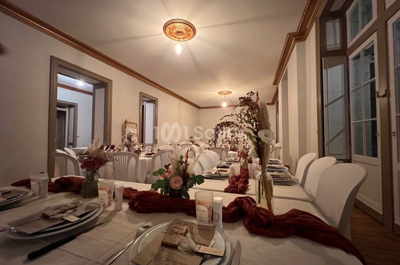 Salle de réception décorée avec des tables dressées, nappes blanches, fleurs séchées et lumière tamisée.