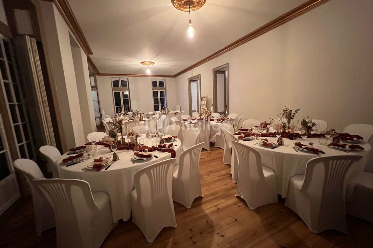 Salle de réception avec tables rondes dressées, nappes blanches, chaises en plastique et décorations florales.