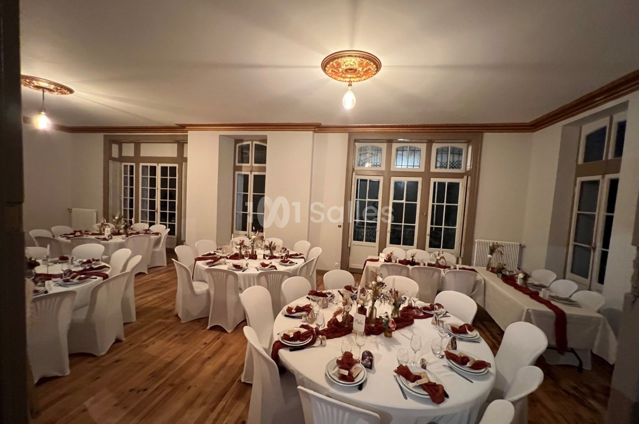 Salle de réception décorée avec des tables rondes, nappes blanches, serviettes rouges et centre de table floral.