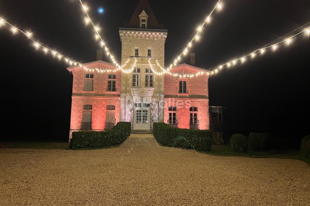 Façade d'un château éclairé par des guirlandes lumineuses et des projecteurs rouges, de nuit.