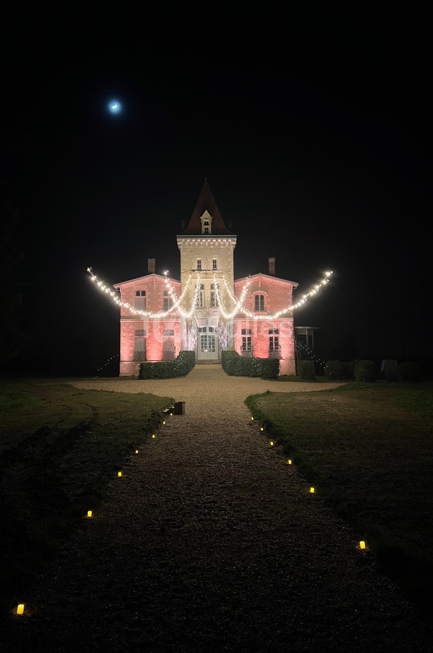 Façade d'un château éclairée par des guirlandes lumineuses, avec un chemin bordé de petites lumières sous un ciel nocturne.