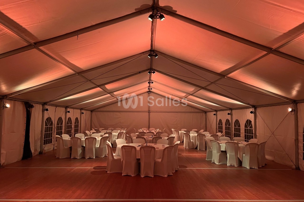 Intérieur d'une tente éclairée en rouge, avec des tables rondes et des chaises blanches disposées pour un événement.