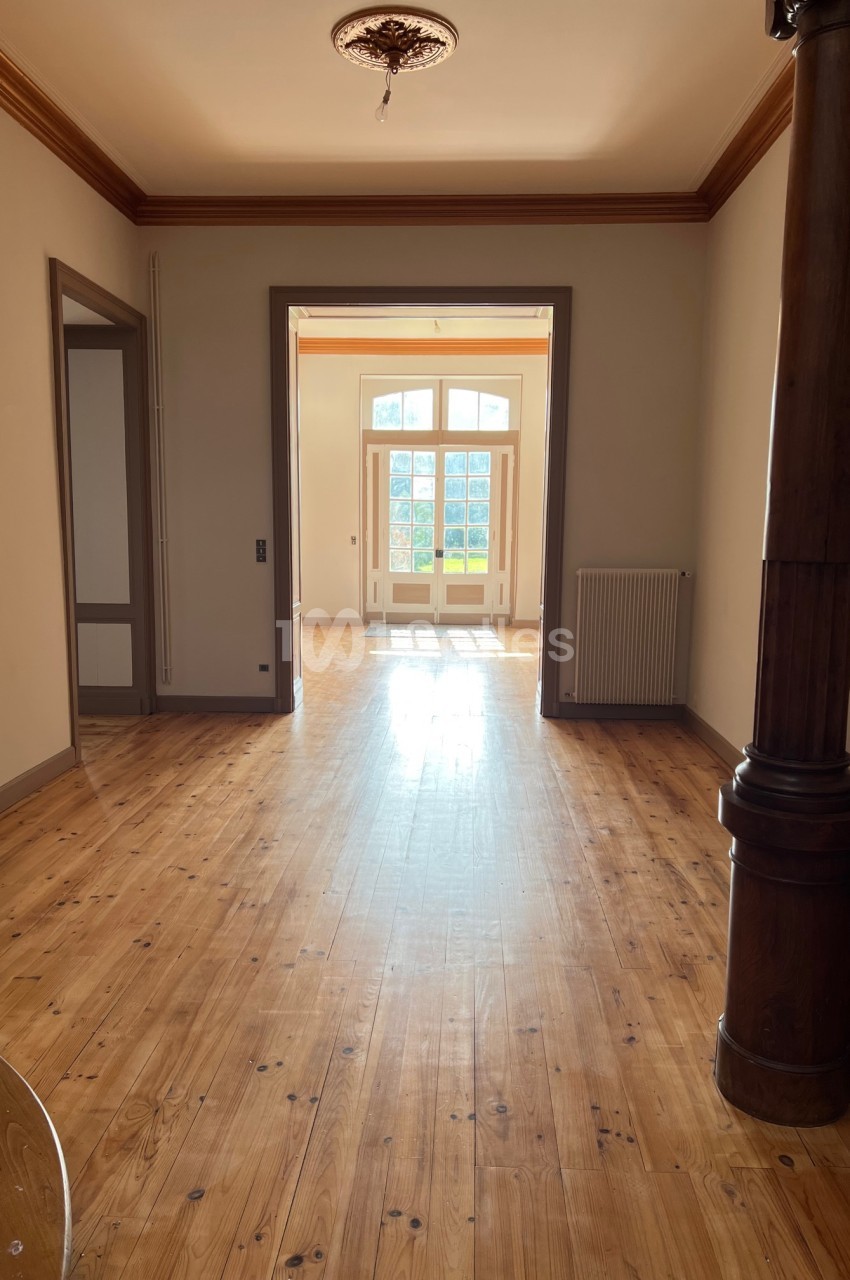 Couloir lumineux avec parquet en bois, ouvert sur une porte vitrée donnant sur un espace extérieur ensoleillé.