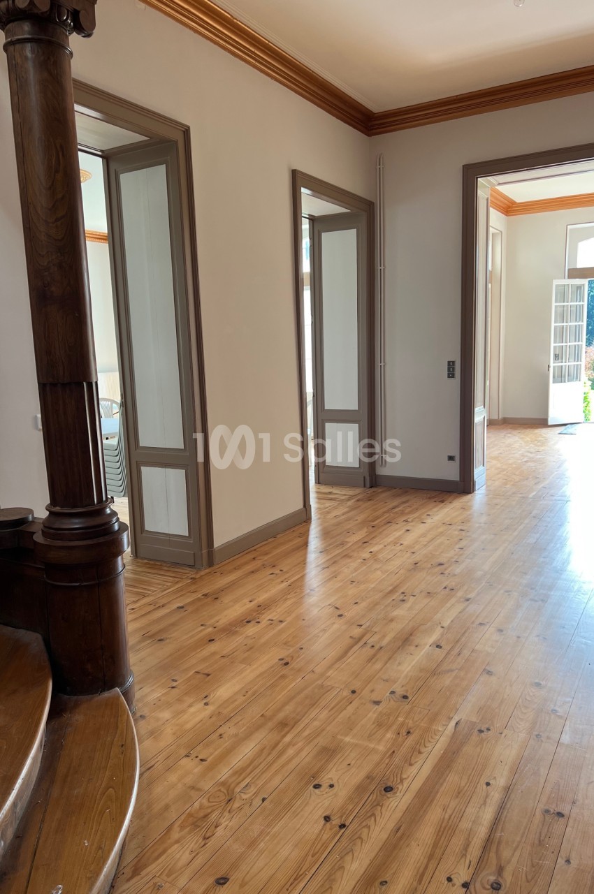 Intérieur lumineux avec parquet en bois, portes ouvertes sur un jardin et escalier en bois au premier plan.