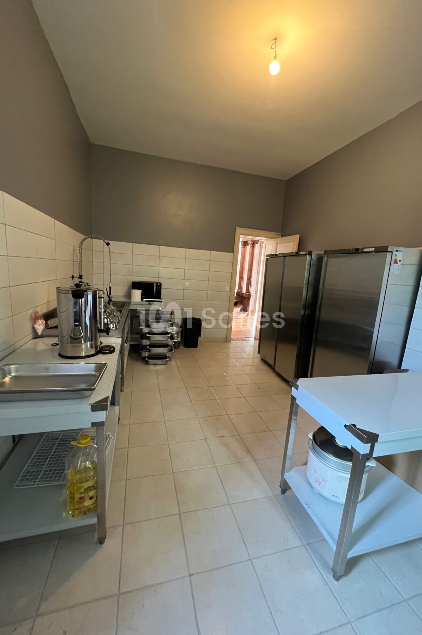Cuisine professionnelle avec carrelage clair, équipements en inox, plan de travail, évier et réfrigérateurs alignés.