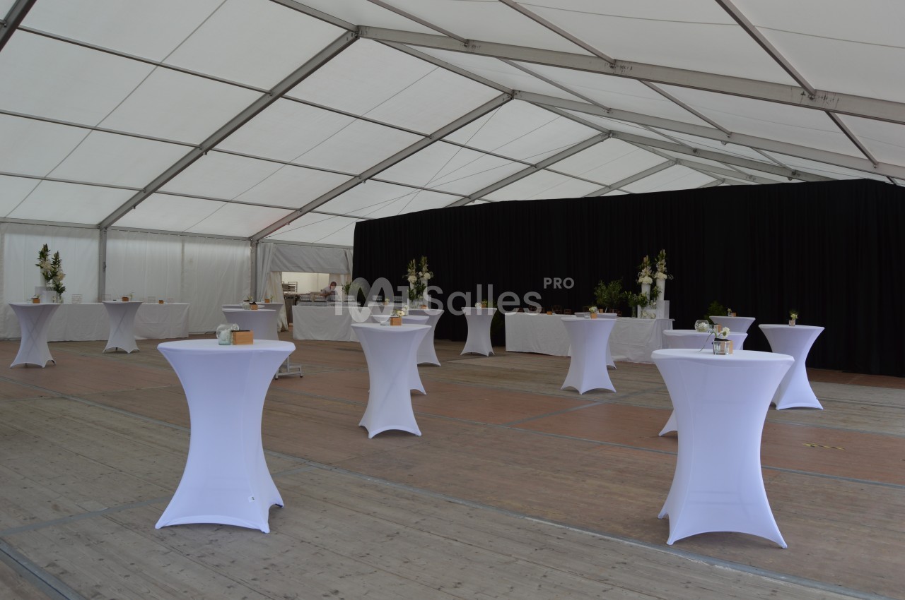 Intérieur d'une tente événementielle avec des tables hautes drapées de blanc et un fond de rideaux noirs.