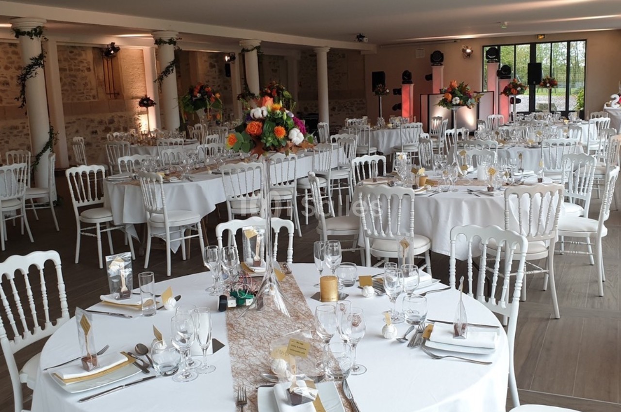 Salle de réception décorée avec des tables rondes dressées, ornées de fleurs colorées et de nappes blanches.