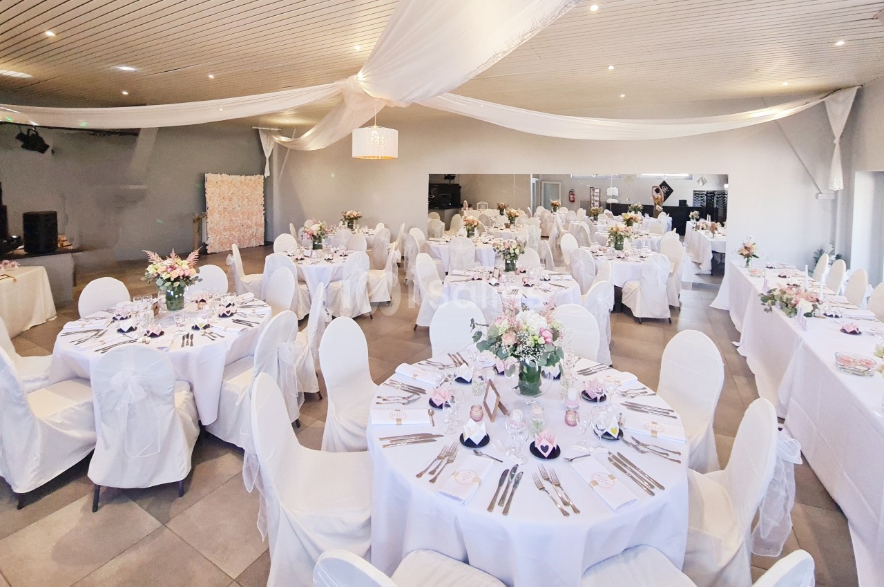 Salle de réception décorée avec des tables rondes dressées, nappes blanches et arrangements floraux.