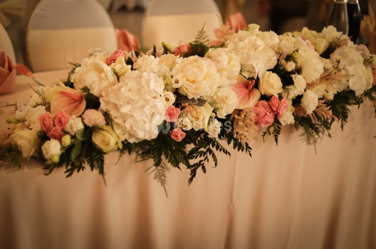 Arrangement floral avec des roses, des hortensias et des feuillages, disposé sur une table recouverte d'une nappe beige.