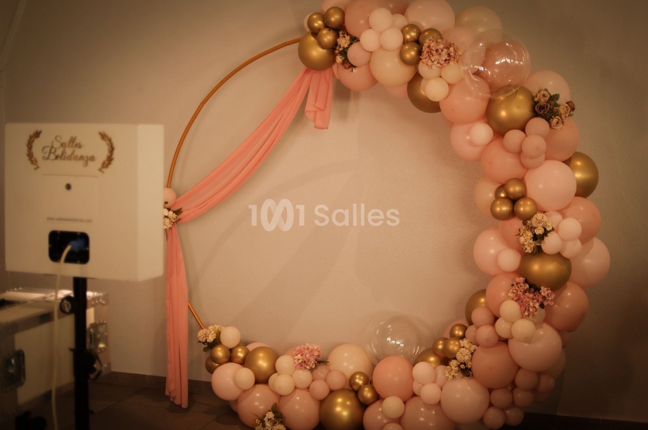 Cercle décoratif en ballons roses, dorés et blancs avec fleurs, installé dans une salle pour un événement.