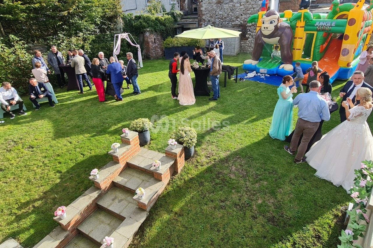 Groupe de personnes rassemblées dans un jardin pour une fête, avec une structure gonflable et des décorations florales.