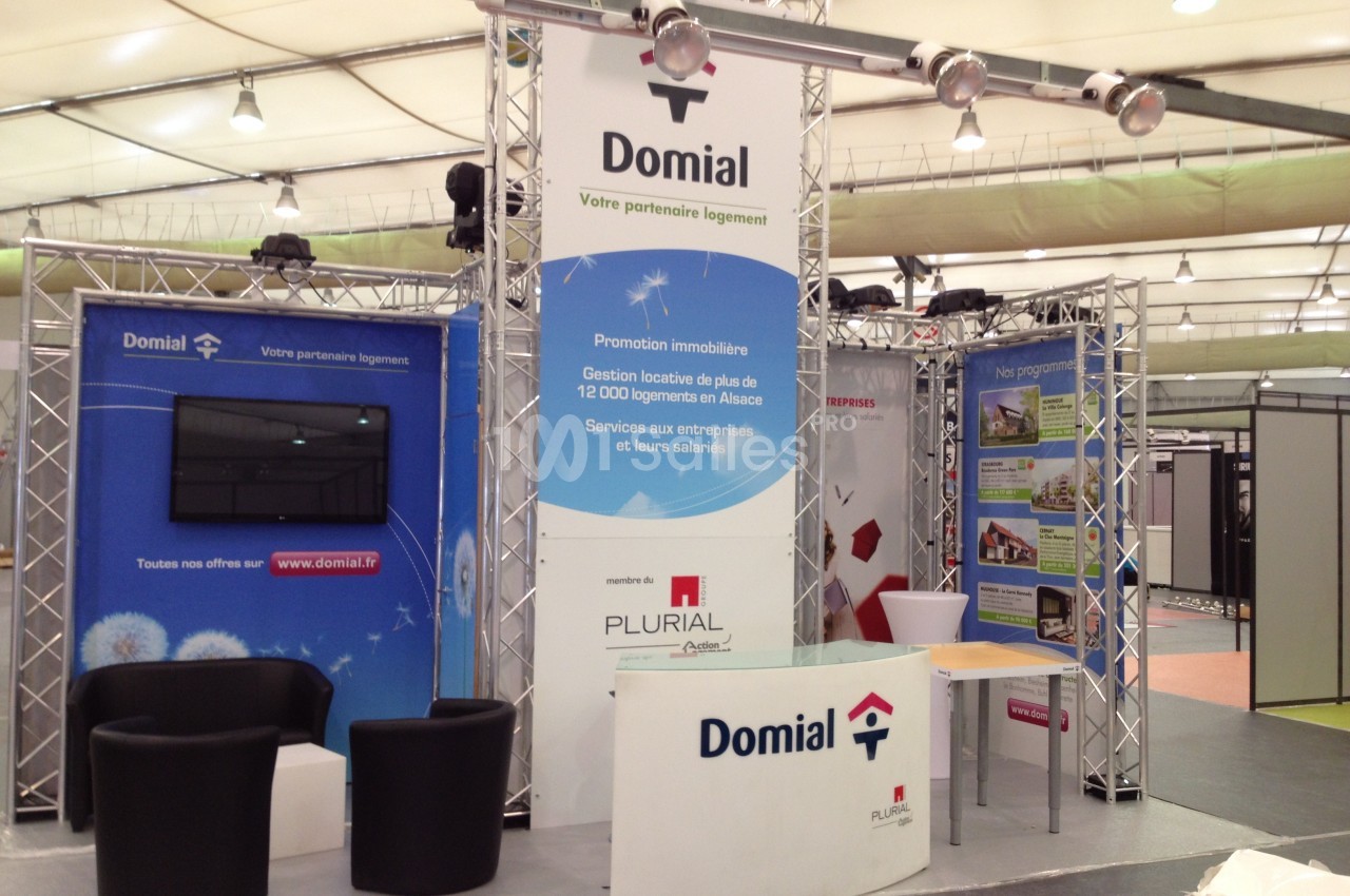 Stand d'exposition avec affiches promotionnelles, mobilier et écran, représentant une entreprise immobilière.