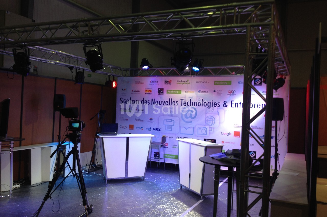 Scène d'exposition avec éclairage, caméras et fond affichant des logos d'entreprises technologiques.