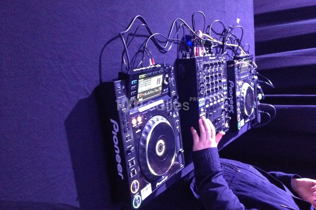 Un DJ manipule une table de mixage et des platines Pioneer sur une surface noire.